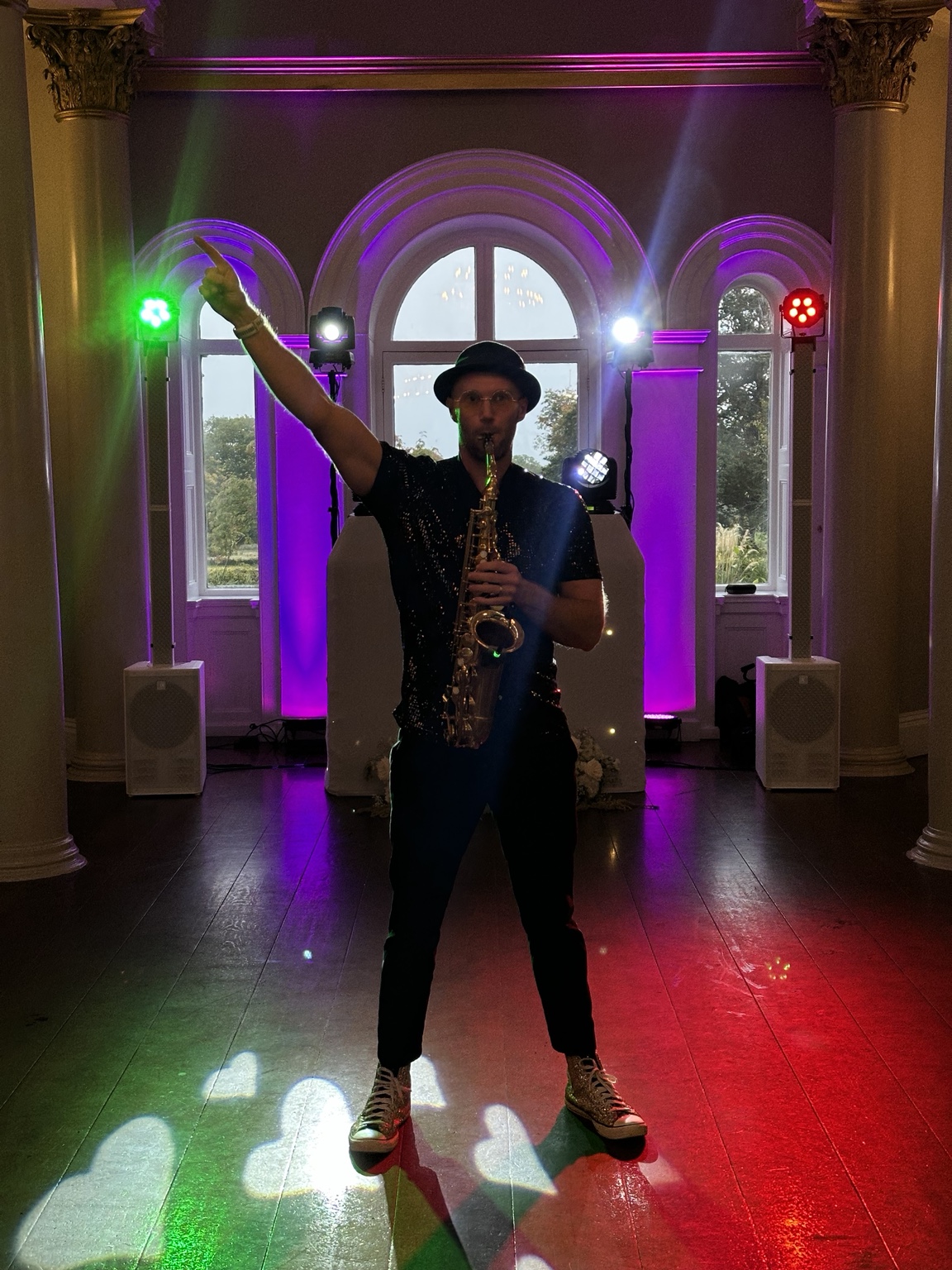 Spencer holding his saxophone beneath colourful evening lights at Lartington Hall