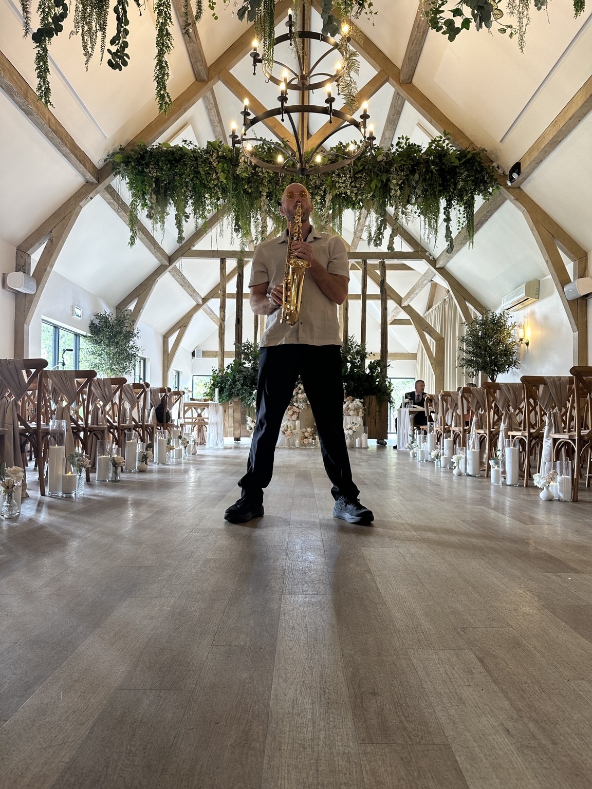 Spencer holding his sax beneath the beams and greenery at The River Barn