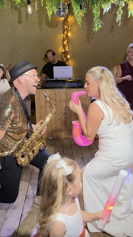 Claire playing an inflatable sax beside Spencer, with DJ Dave Taylor behind the booth