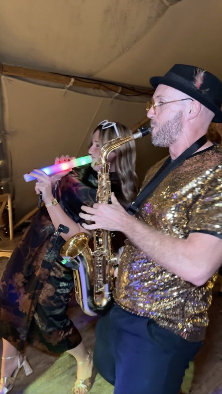 Spencer playing sax beside a wedding guest holding a light-up baton