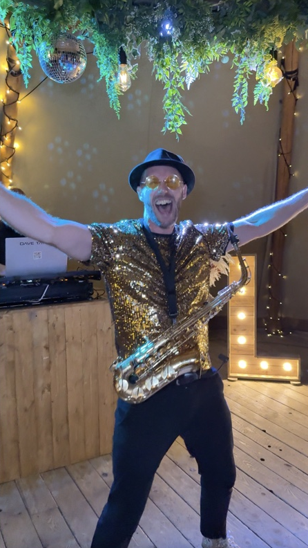 Spencer celebrating with his saxophone beneath foliage and disco balls in the tipi