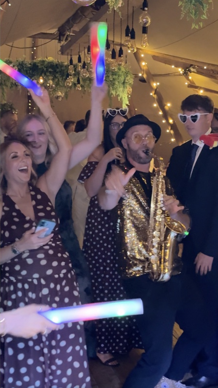 Spencer playing sax among guests waving light-up batons inside the wedding tipi
